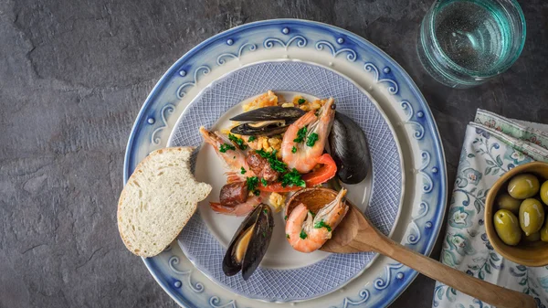 Plate with paella on the dark stone table with different accessories top view — стоковое фото