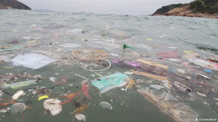 A surgical mask floats in the sea among dense plastic pollution